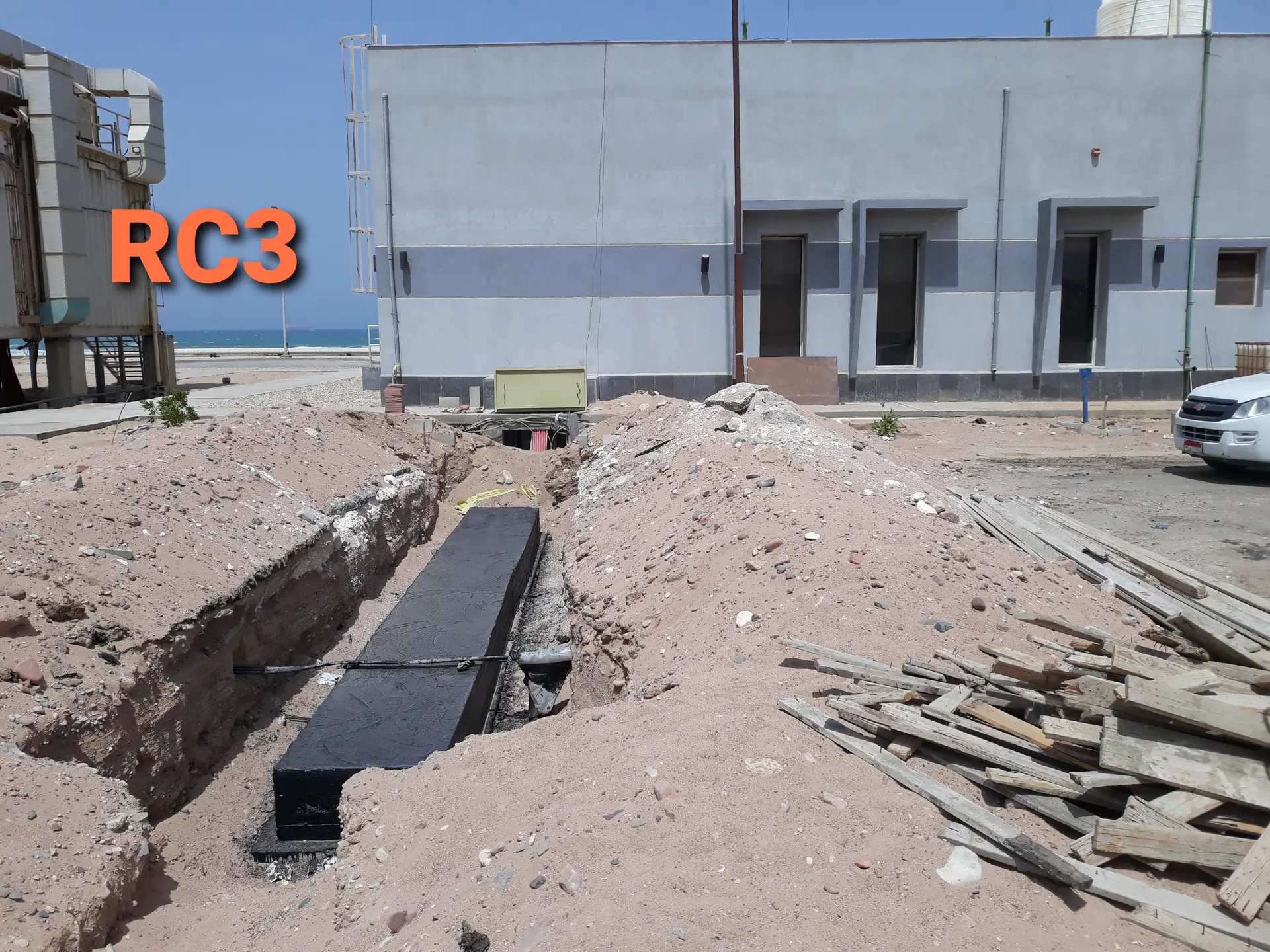 Excavated cable trench beside a plant building